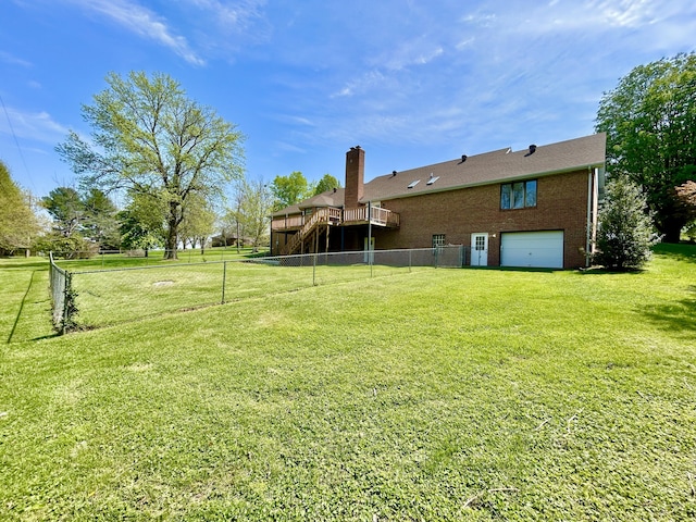 view of yard with an attached garage, a wooden deck, driveway, and fence