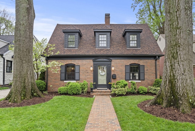 view of front of house with a front yard, a chimney, a shingled roof, and brick siding