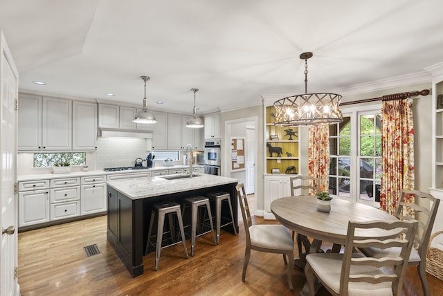 kitchen featuring a sink, gas cooktop, light wood finished floors, a notable chandelier, and backsplash