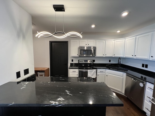 kitchen with dark wood-style flooring, dark stone counters, white cabinetry, a sink, and appliances with stainless steel finishes
