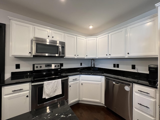 kitchen featuring a sink, dark stone counters, stainless steel appliances, white cabinetry, and dark wood-style floors