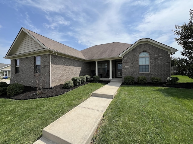 ranch-style home with covered porch, a shingled roof, a front lawn, and brick siding