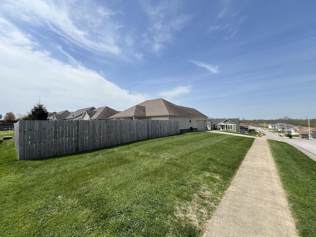 view of yard featuring an attached garage, fence, and a residential view