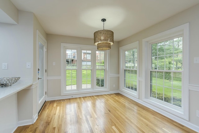 unfurnished dining area featuring a wealth of natural light, an inviting chandelier, light wood-style floors, and visible vents