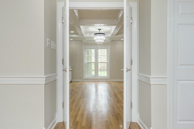 hallway with baseboards, ornamental molding, a chandelier, wood finished floors, and coffered ceiling