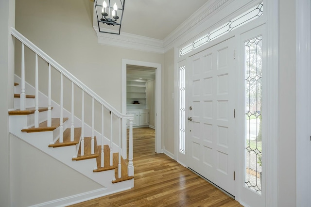 foyer featuring a chandelier, stairs, ornamental molding, and wood finished floors