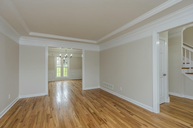 spare room featuring an inviting chandelier, ornamental molding, visible vents, stairway, and light wood finished floors