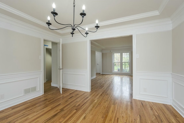 unfurnished dining area featuring ornamental molding, visible vents, light wood-style flooring, and an inviting chandelier