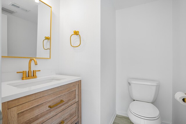 bathroom featuring baseboards, vanity, toilet, and visible vents