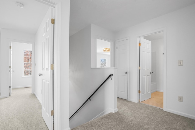 hall with light colored carpet, baseboards, a wealth of natural light, and an upstairs landing