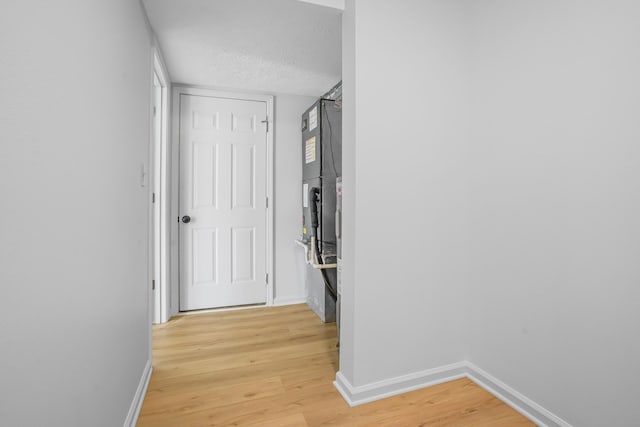 hall with baseboards, a textured ceiling, and light wood-type flooring