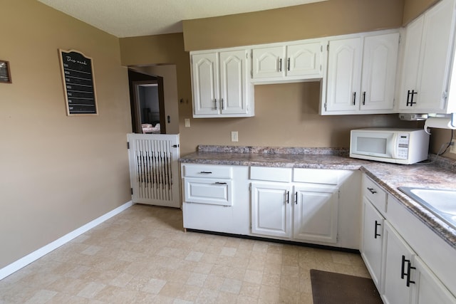 kitchen with a sink, white microwave, white cabinetry, and baseboards