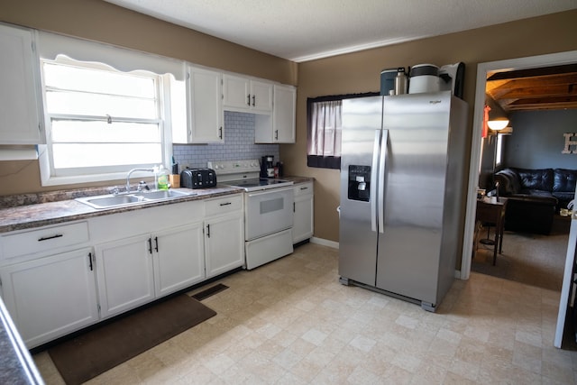 kitchen with visible vents, white cabinets, stainless steel fridge, a sink, and white electric range oven
