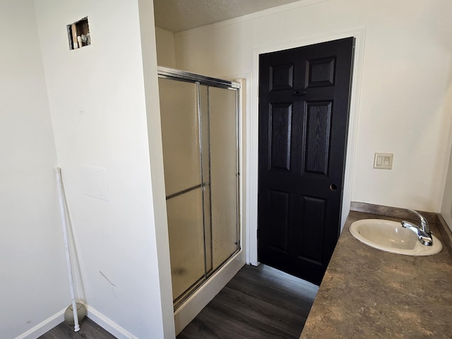 bathroom featuring baseboards, wood finished floors, a sink, and a stall shower