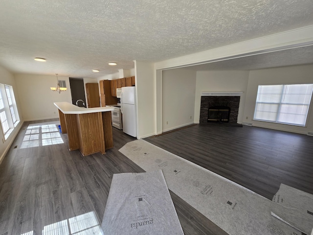 unfurnished living room featuring a textured ceiling, dark wood-style flooring, baseboards, a notable chandelier, and a fireplace
