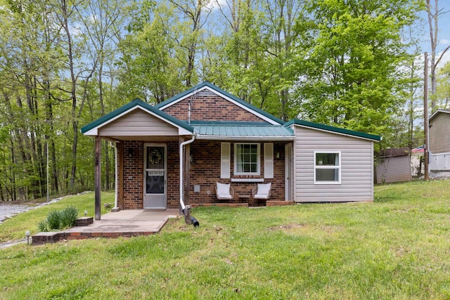 view of front facade with a front lawn, brick siding, metal roof, and covered porch