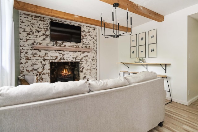 living area with light wood-style flooring, beamed ceiling, a fireplace, baseboards, and a notable chandelier