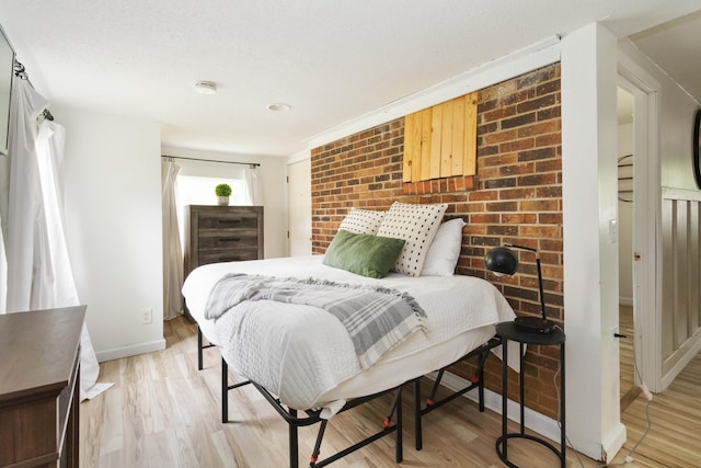 bedroom with brick wall, baseboards, and light wood-style floors
