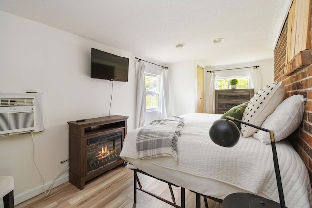 bedroom featuring light wood-style flooring, baseboards, a wall mounted AC, and a lit fireplace