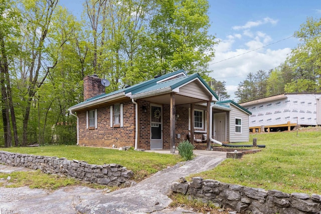 view of front of home featuring a front lawn, a chimney, covered porch, and brick siding