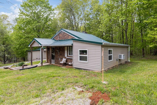 view of front of property featuring covered porch, a wall unit AC, a front lawn, and metal roof