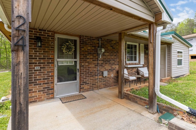 view of exterior entry with brick siding and a porch