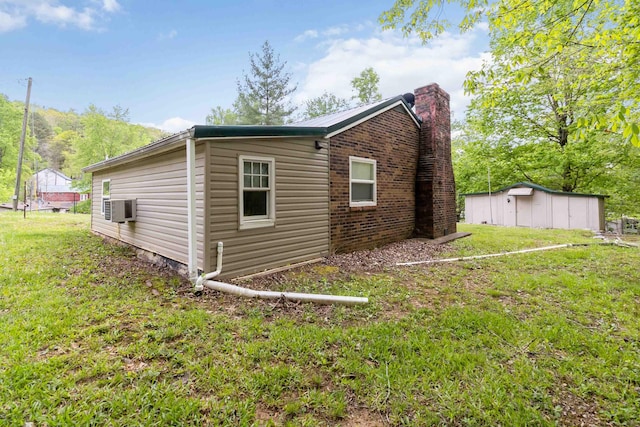 view of home's exterior with a chimney, a yard, cooling unit, an outdoor structure, and a storage unit