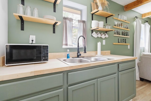 kitchen featuring open shelves, a sink, black microwave, light wood finished floors, and beamed ceiling