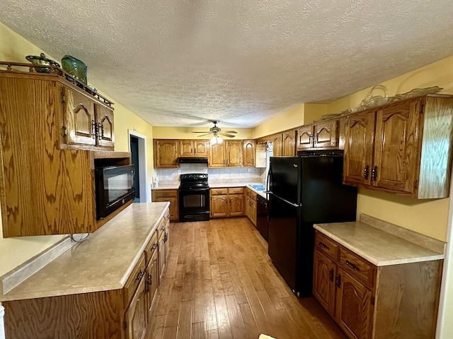 kitchen featuring brown cabinetry, black appliances, a textured ceiling, and light countertops