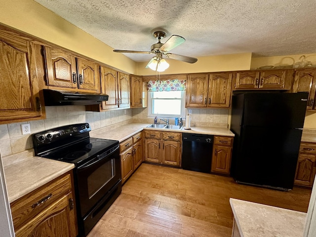kitchen featuring brown cabinetry, under cabinet range hood, black appliances, a sink, and a ceiling fan