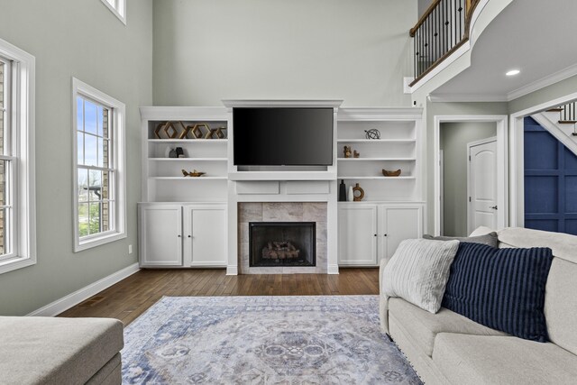 living room with stairway, wood finished floors, crown molding, baseboards, and a tiled fireplace