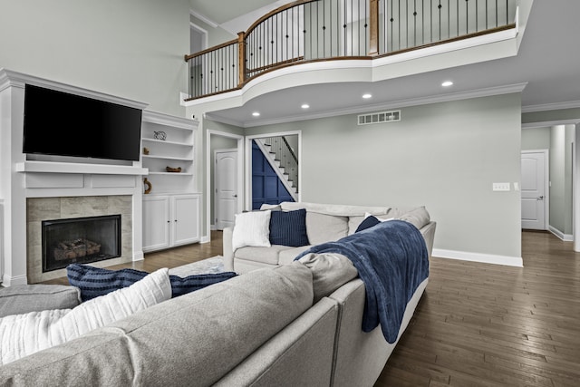 living area featuring crown molding, a tile fireplace, wood-type flooring, a high ceiling, and visible vents