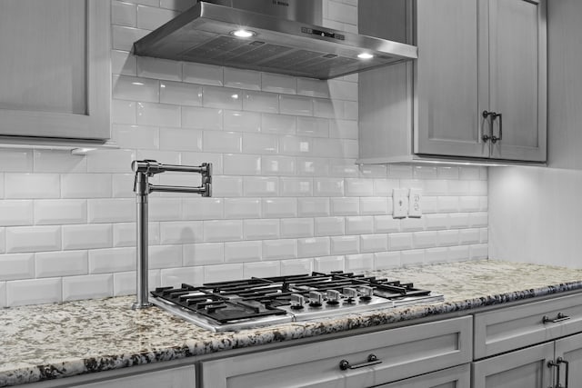 kitchen with light stone countertops, decorative backsplash, stainless steel gas cooktop, and extractor fan