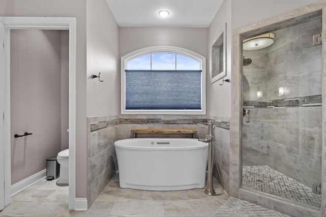 bathroom with a wainscoted wall, toilet, tile walls, a soaking tub, and a stall shower