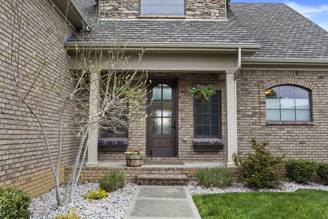 property entrance featuring a shingled roof and brick siding