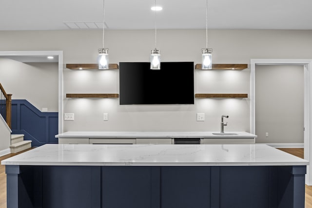 kitchen with light wood finished floors, a sink, visible vents, light stone counters, and hanging light fixtures