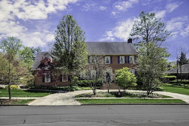 colonial-style house featuring driveway, a chimney, and a front yard