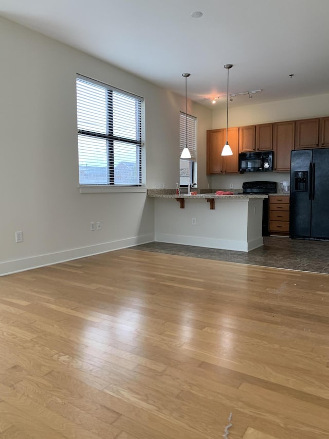 650 S Mill St Unit 218, Lexington, KY 40508 - kitchen featuring black appliances, wood finished floors, brown cabinetry, hanging light fixtures, and a kitchen breakfast bar