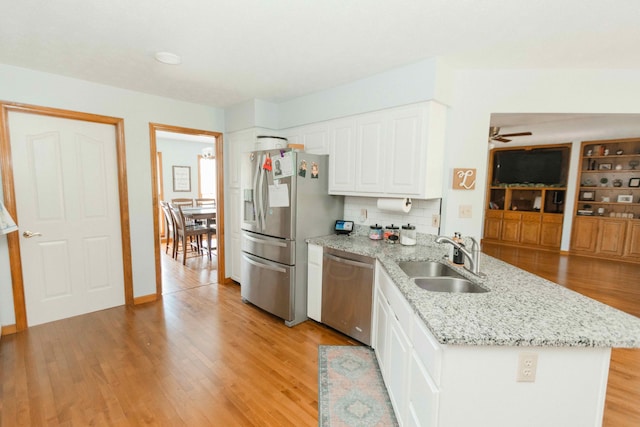 kitchen with white cabinets, stainless steel appliances, a peninsula, a sink, and light wood-type flooring