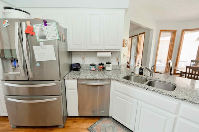 kitchen with light stone counters, a sink, light wood-style flooring, appliances with stainless steel finishes, and white cabinetry