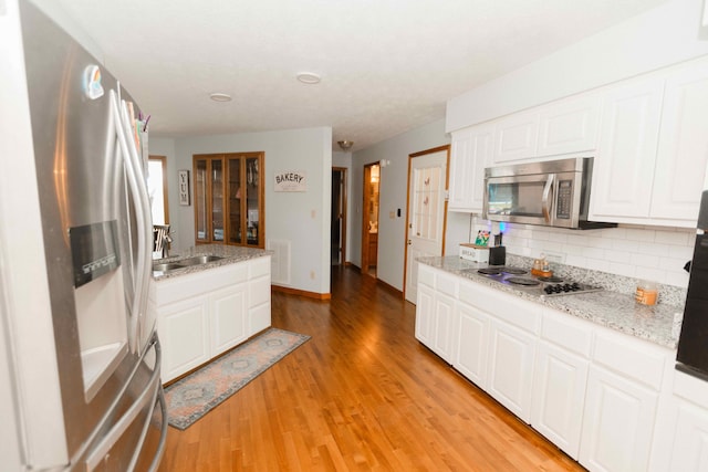 kitchen with light wood finished floors, white cabinets, a sink, decorative backsplash, and appliances with stainless steel finishes