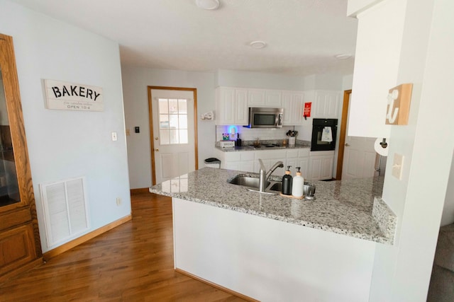 kitchen with wood finished floors, visible vents, stainless steel microwave, a peninsula, and white cabinetry