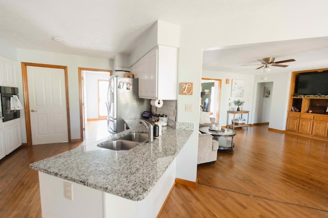 kitchen with a sink, oven, light wood-type flooring, white cabinets, and freestanding refrigerator
