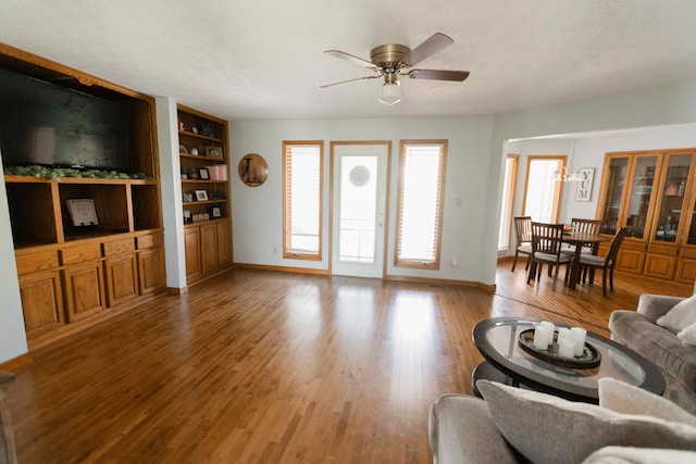 living room featuring light wood-type flooring, built in shelves, baseboards, and ceiling fan