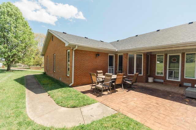 back of property featuring a lawn, roof with shingles, brick siding, and a patio area