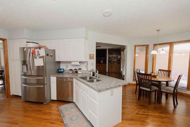 kitchen with a peninsula, stainless steel appliances, light wood-type flooring, and a sink