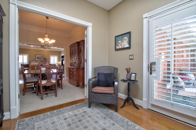 sitting room with baseboards, ornamental molding, wood finished floors, and a notable chandelier