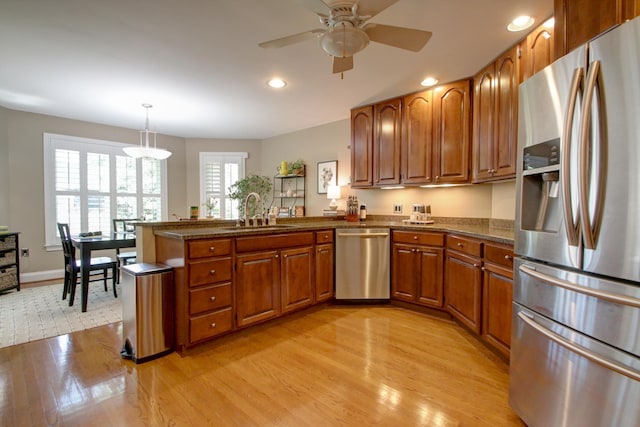kitchen with brown cabinetry, a peninsula, light wood-style floors, a sink, and appliances with stainless steel finishes