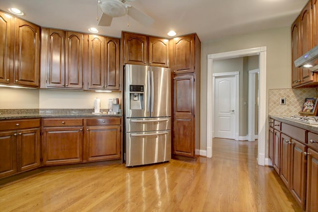 kitchen with backsplash, a ceiling fan, appliances with stainless steel finishes, brown cabinets, and light wood-style flooring