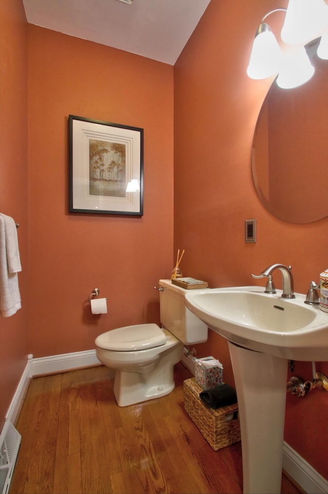 half bath featuring a sink, toilet, baseboards, wood finished floors, and visible vents